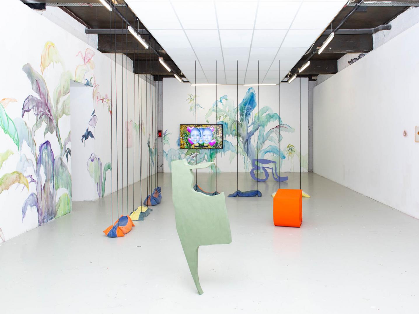 An exhibition room with several colourful objcets, a video screen and flowery wallpaper at the GENERATOR exhibition at EESAB in Quimper, France