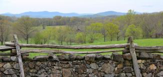 An idyllic view on a rural valley with in the foreground a wooden fence and in the back a mountain range.