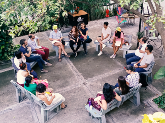 A group of people sitting outside in a circle surrounded by plants