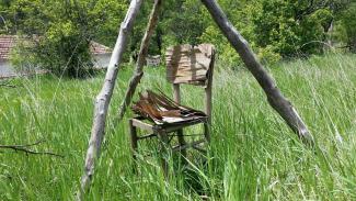 A wooden chair in a grass field arched by wooden sticks.