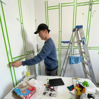 An artist sticking green tape to the walls in an act of preparing the white walls of the studio for an exhibition.