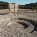 A circle of rocks in a desert with a wooden trellis in the background