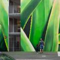 A man and a child viewing a green mural depicting plants in public space.