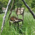 A wooden chair in a grass field arched by wooden sticks.