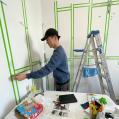An artist sticking green tape to the walls in an act of preparing the white walls of the studio for an exhibition.