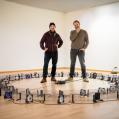 Two people in the midst of their art installations in an exhibition room, looking at the camera