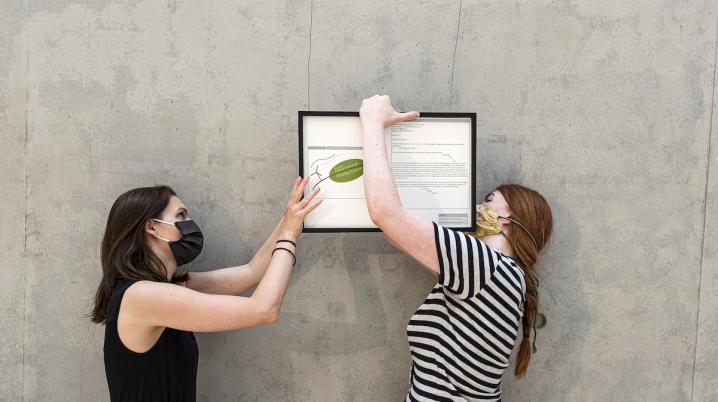 two women wearing facemasks holding a work a art against a grey wall in Cité Internationale des Arts, France