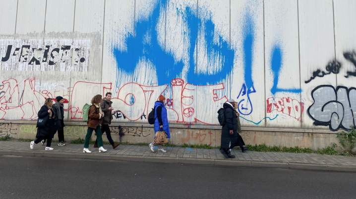 a group of people walking on the street besides a wall with graffiti on it.
