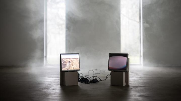Two screens depicting a video shown in a smoky exhibition space.