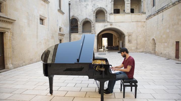 Aman playing a grand piano in the courtyard of KORA Contemporary Arts Center in Puglia, Italy