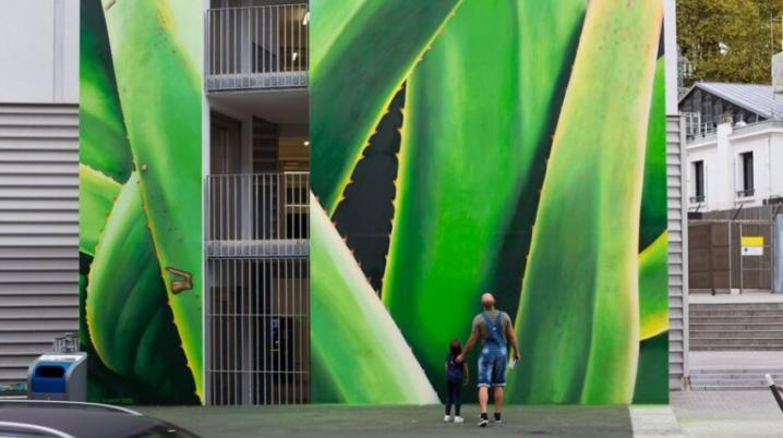 A man and a child viewing a green mural depicting plants in public space.