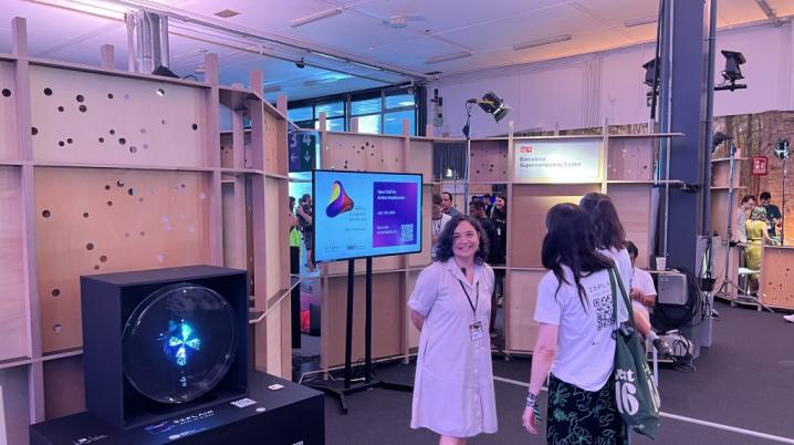 A group of women in an exhibition space made of wooden panels and television screens.