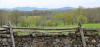 An idyllic view on a rural valley with in the foreground a wooden fence and in the back a mountain range.