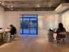 Two persons working in a warmly lit gallery space with a door leading to a neighborhood street