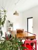 A wooden dinner table in a white room with plants and a ceiling lamp.